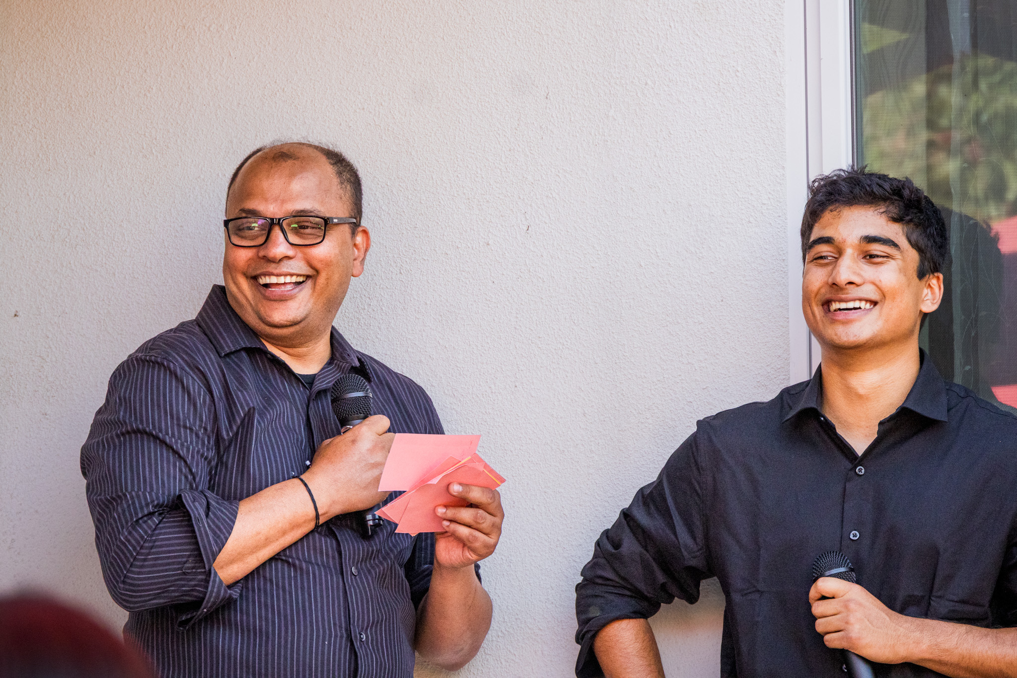 Older and younger man smiling while speaking into microphones