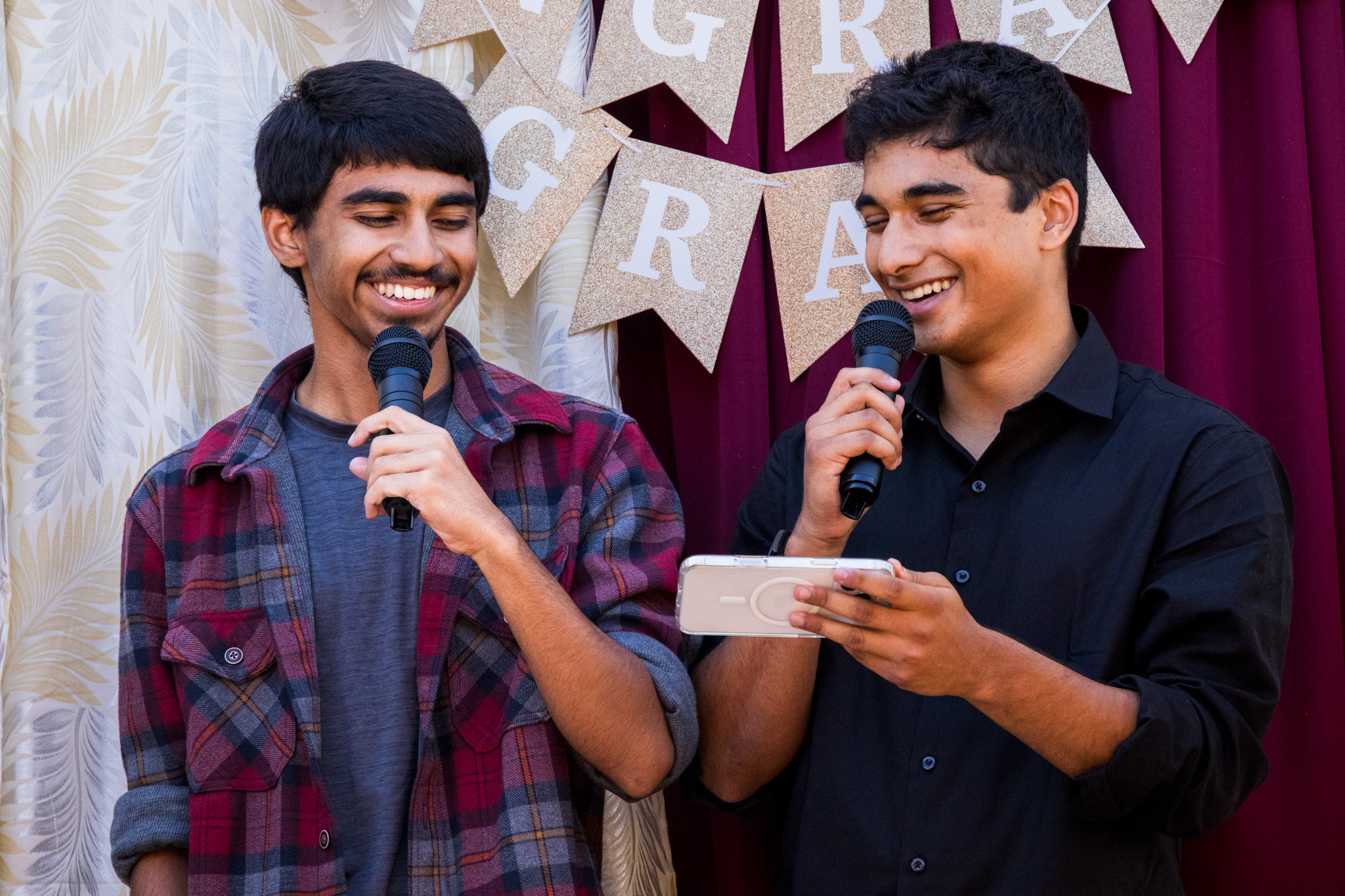 Two young men smiling at each other while speaking into microphones